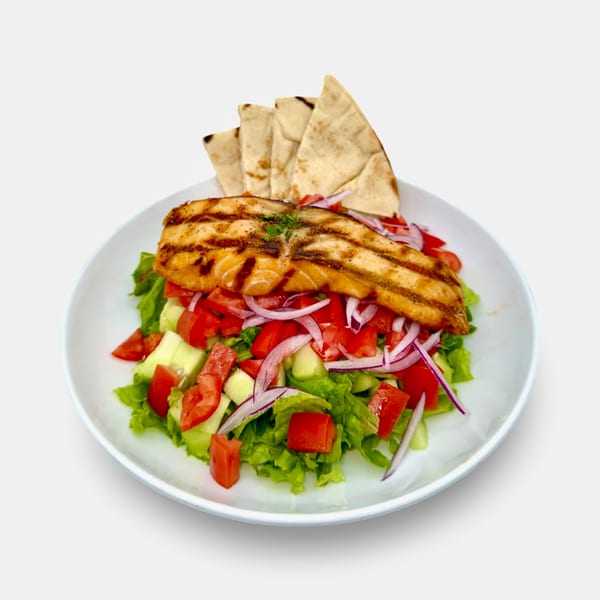 Grilled salmon over a fresh Mediterranean salad with pita bread on a white plate.