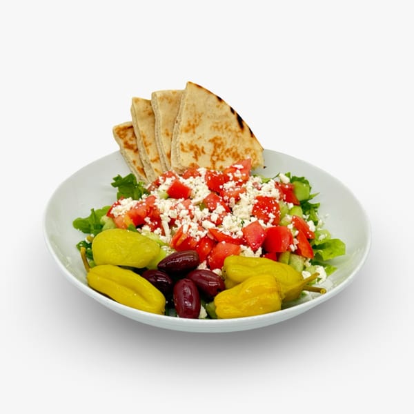 Mediterranean salad with lettuce, tomatoes, feta, olives, peppers, and pita bread in a white bowl.