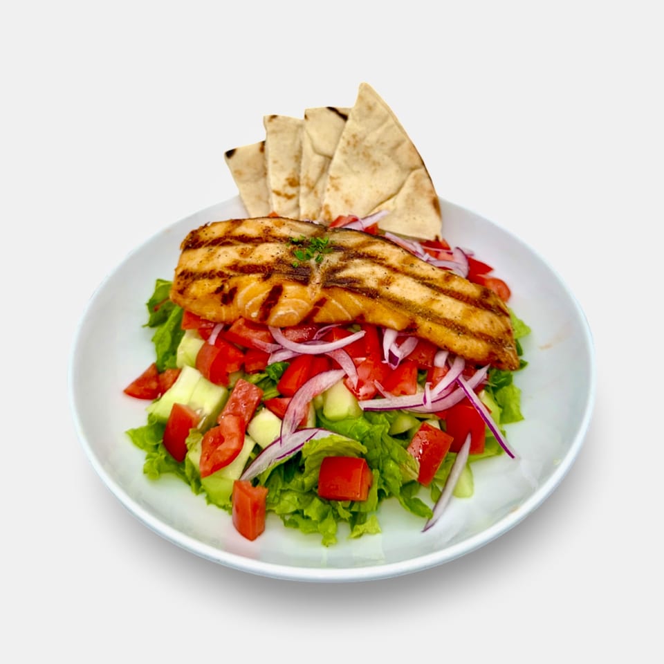 Grilled salmon over a fresh Mediterranean salad with pita bread on a white plate.